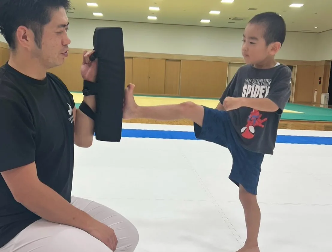 支部長がミットを構え、体験に来た子どもが蹴りを出すところ